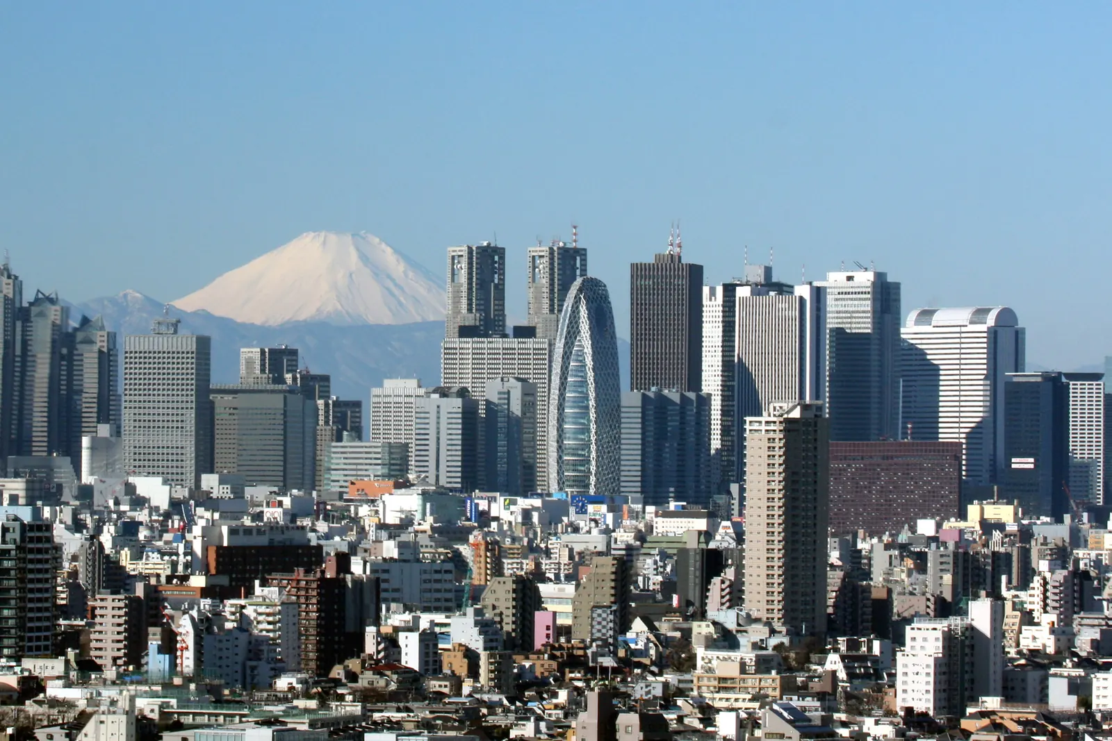Skyscrapers of Shinjuku, Tokyo, stand over low buildings with Mount Fuji snow-capped on the horizon
